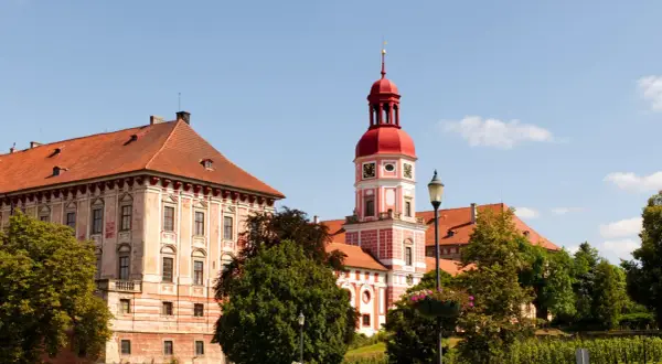 Schloss Roudnice nad Labem mit seinem roten Turm und den Ziegeldächern, umgeben von grünen Bäumen.
