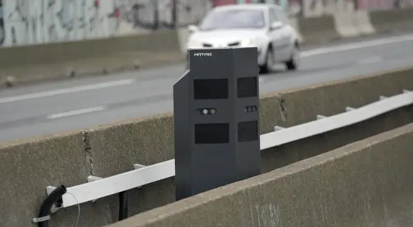 Un nouveau radar noir surveille la route. Une voiture passe en arrière-plan.