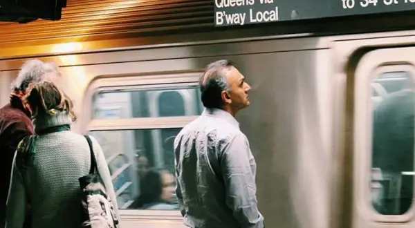 Personas esperando un tren en el metro de Nueva York con un letrero de destino.
