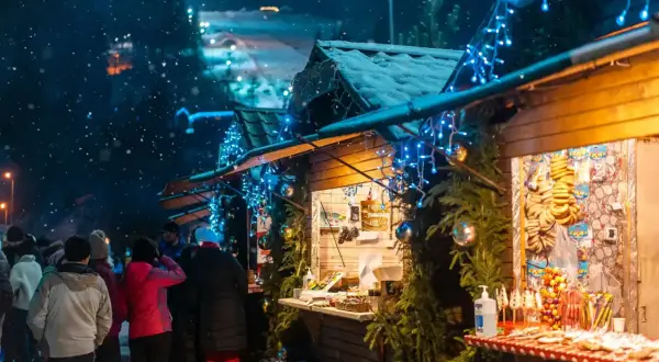 Mercatini di Natale nelle Marche: bancarelle illuminate da lucine blu, neve che cade e gente che passeggia tra gli stand.