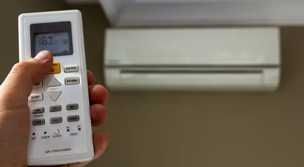 Mano che regola il telecomando del condizionatore, impostando la temperatura. Scopri quanto consuma un condizionatore per un comfort ottimale.