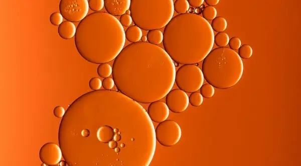 Orangefarbene Bläschen, wie von Butylmethoxydibenzoylmethan, schweben auf einem warmen, orangen Hintergrund.