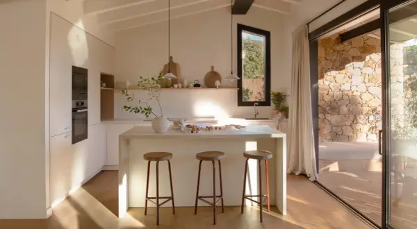 Cocina luminosa con isla central, taburetes y vistas a un patio de piedra, ideal para casas de campo modernas.