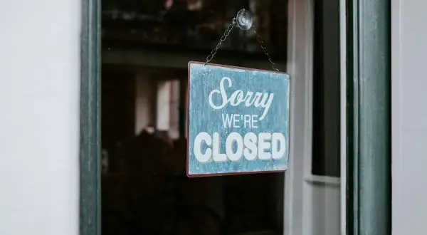 En blå skylt med texten "Sorry WE'RE CLOSED" hänger i ett fönster. Enskild firma i vilande.