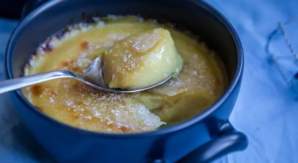 En sked lyfter en bit av krämig, karamelliserad vegansk creme brulee ur en mörkblå skål.
