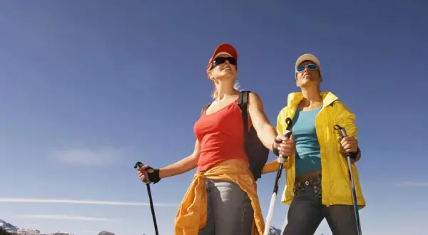 Dwie kobiety z kijkami do nordic walking podziwiają górski krajobraz.