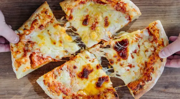 New York Style Pizza mit geschmolzenem Käse, von Händen gehalten, auf Holzuntergrund.