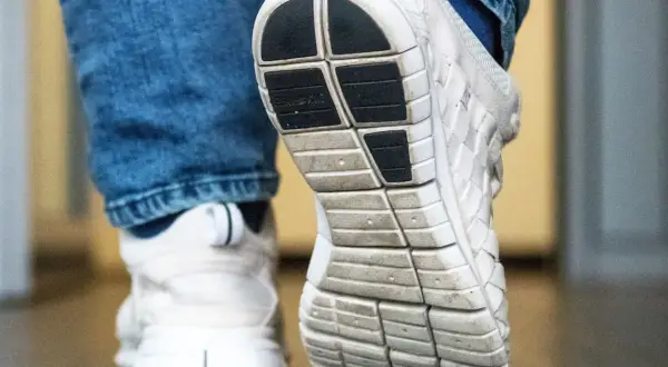 Nahaufnahme von weißen Turnschuhen mit Jeans. Die Sohle eines Schuhs ist deutlich zu sehen, bereit für den nächsten Schritt, der vielleicht quietschende Schuhe hinterlässt.