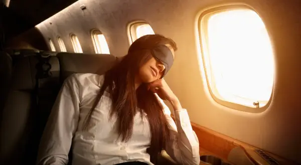 Frau mit Schlafmaske im Flugzeug, um Jetlag zu vermeiden.