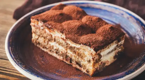 Pyszny kawałek tiramisu na talerzu, posypany kakao. Zastanawiasz się, jaki alkohol do tiramisu nada mu idealny smak?