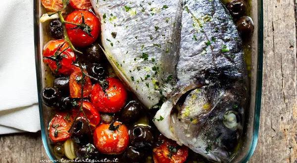 Orata al forno con pomodorini, olive nere e aglio, un piatto semplice e gustoso pronto per essere infornato.
