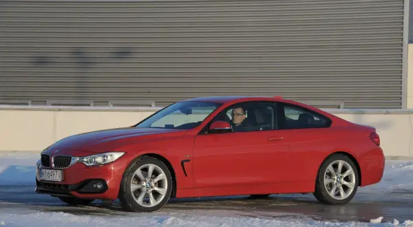 Czerwone BMW F32 435i z kierowcą za kierownicą, zaparkowane na śniegu przed budynkiem.