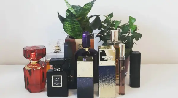 Kolekcja perfum: czerwony Chopard, czarny Coco Noir Chanel 100ml, fioletowy i złoty Michael Kors, oraz inne, otoczone zielenią.