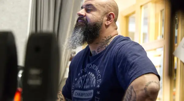 Man med skägg och tatueringar, klädd i en t-shirt med texten "Performance First Session Championship". Kanske en del av "kaka kartellen" som förbereder sig för något.
