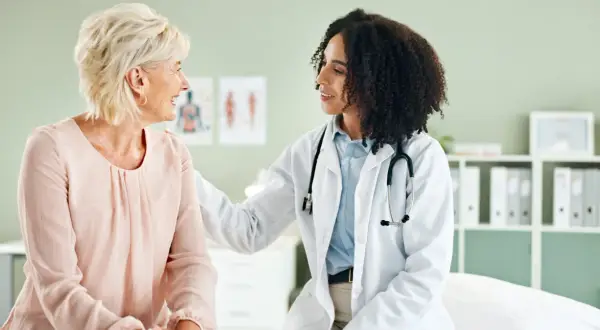 Ärztin mit Stethoskop legt Hand tröstend auf Schulter einer Patientin. Ein Gespräch über gynäkoonkologische Themen findet in einer freundlichen Atmosphäre statt.