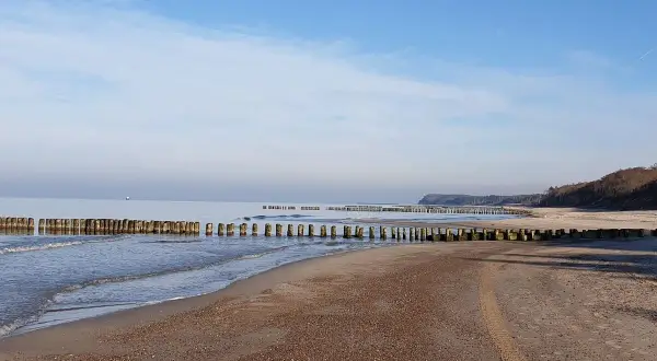 Spokojne morze i pusta plaża w Rusinowie nad morzem. Drewniane falochrony wcinają się w wodę, tworząc malowniczy krajobraz.