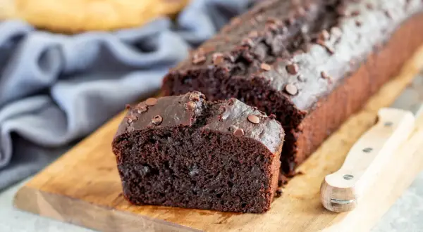 Fetta di banana al cioccolato, soffice e ricca, con gocce di cioccolato fondente, su tagliere di legno.