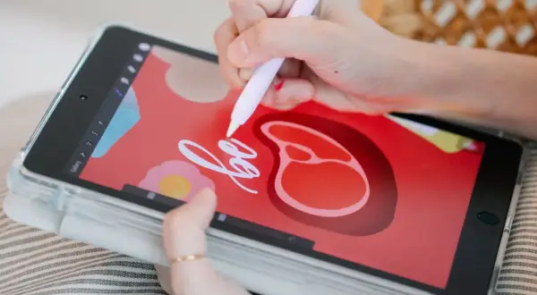 Rysowanie na tablecie za pomocą rysika w aplikacji do rysowania. Na ekranie widać czerwone tło z grafiką steka i kwiatka.
