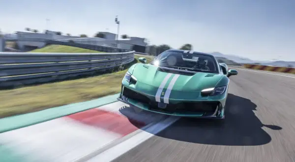 Zielony Ferrari 296 GTB z białymi pasami pędzi po torze wyścigowym, zostawiając za sobą rozmyte tło.