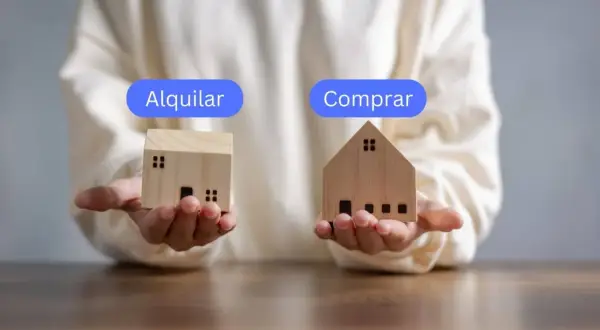 Manos sostienen casas de madera, una con "Alquilar" y otra con "Comprar", para decidir qué es mejor comprar o alquilar.