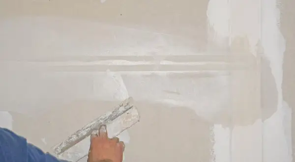 Hand spachtelt eine Rigips-Wand glatt. Die Naht wird mit Spachtelmasse bedeckt, um eine ebene Oberfläche für die weitere Bearbeitung zu schaffen.