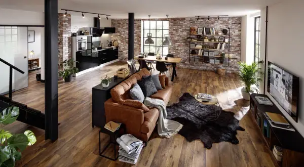 Geräumiges Wohnzimmer im industrial style mit brauner Ledercouch, Holztisch und Ziegelwand.