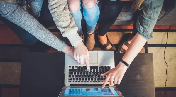 Flera personer pekar på en laptop och en surfplatta, ett tydligt exempel på delaktighet i ett projekt.