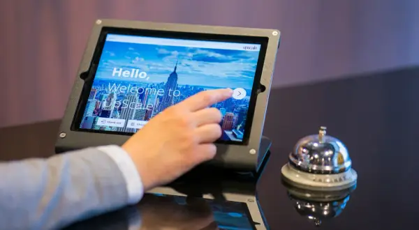 Dłoń dotyka ekranu tabletu z napisem "Welcome to UpScale". Czy to oznacza, że ile trzeba mieć lat żeby zameldować się w hotelu?