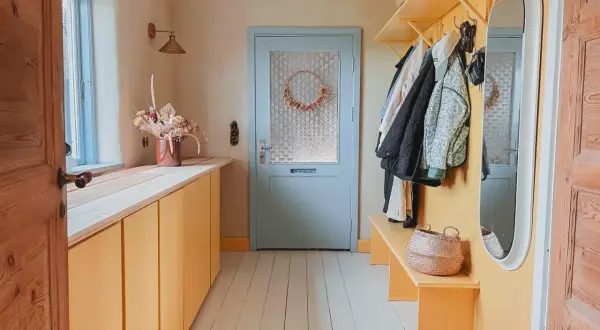 Warme Farben und natürliche Materialien prägen diesen Flur. Farbgestaltung Flur Tapeten Beispiele: Gelbe Schränke, Holzboden, Garderobe mit Jacken.