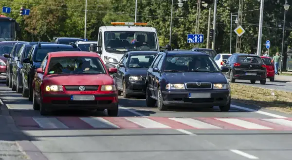 Korki na drodze, kierowcy próbują omijanie stojących aut. Czerwony Volkswagen i granatowa Skoda czekają na zielone światło.