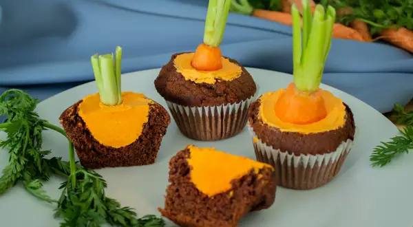 Schokoladen-Muffins mit orangefarbener Glasur und einem kleinen Karottenstück mit Grün als Osterdekoration.