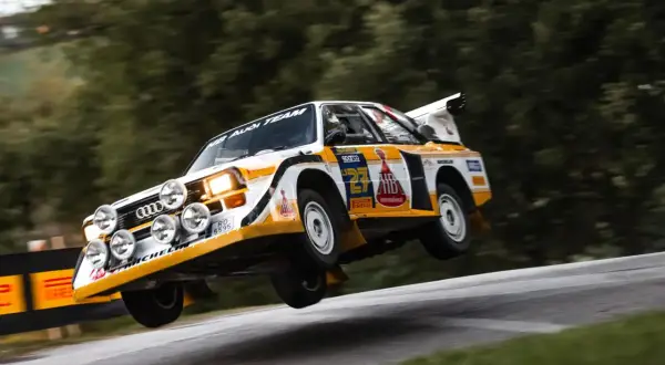 Audi Sport Quattro w akcji, pokonuje nierówność drogi, unosząc się w powietrzu.