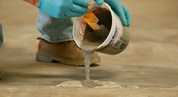 Man con guantes azules vierte mortero para reparación de fisuras en soleras de hormigón.