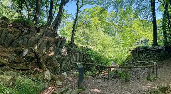 Ein Pfad führt durch einen Wald mit steilen Felsformationen. Ein blauer Stein liegt am Wegesrand.