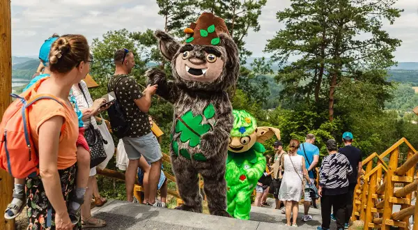 Maskotki w solina park rozrywki witają gości. Wesołe postacie w otoczeniu zieleni i drzew.