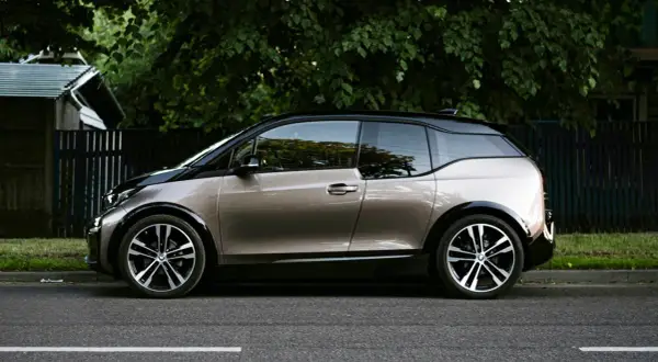 En BMW i3 står parkerad vid en grönskande trädgård. Kanske ett problem med laddningen?