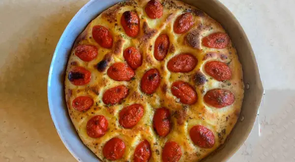Focaccia foggiana dorata e fragrante, con pomodorini succosi e erbe aromatiche, pronta per essere gustata.