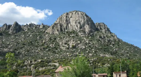 Majestuosa sierra de la Cabrera, con sus rocas imponentes y vegetación verde, bajo un cielo azul con nubes blancas.