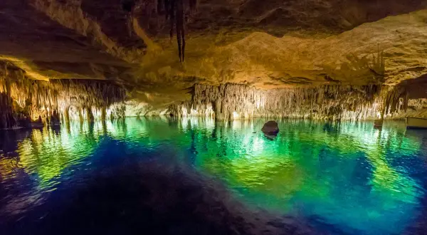 Magiska grottor på Mallorca med turkost vatten som reflekterar stalaktiter och stalagmiter. En båt anas i bakgrunden.