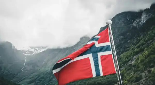 Norweska flaga na tle fiordu. Marzenie o wysokich zarobkach w Norwegii staje się bliższe.