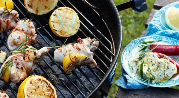 Grillad kyckling med citron och rosmarin på grillen. En tallrik med kycklingröra, chili och örter står bredvid.