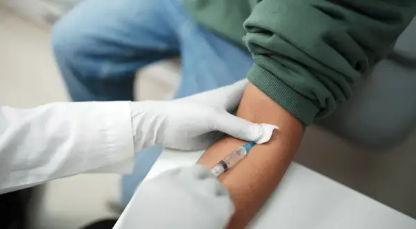 Pobieranie krwi do badań, które mogą pomóc w diagnostyce trzustki. Lekarz w rękawiczkach pobiera krew strzykawką.