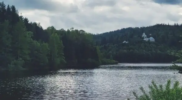 Spokojne jezioro Czerniańskie otoczone gęstym lasem, z widocznym na wzgórzu pałacem.
