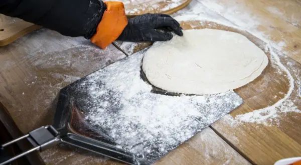 Hand mit Handschuh legt Teig auf bemehltes Pizzaschaufel.