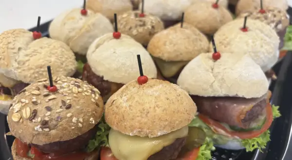 Mini hamburgery gdzie kupić? Taca pełna pysznych, małych burgerów z serem, warzywami i różnymi bułkami. Idealne na imprezę!