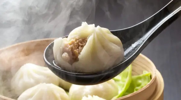 Gorące pierożki dim sum unoszą się w parze, jeden z nich na łyżce odsłania soczyste nadzienie.