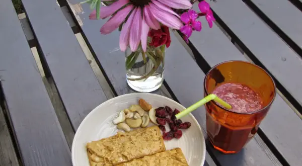 En tallrik med kex med jordnötssmör, nötter och torkade tranbär, samt ett glas smoothie. Perfekt för ett snabbt och gott mellis tips.