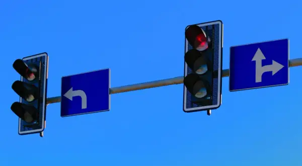 Feu de circulation au dessus d'un panneau bleu indiquant un virage à gauche. Un autre feu de circulation est visible plus loin.