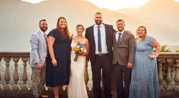 Foto invitati matrimonio: sposi con amici e familiari, con sfondo di montagne al tramonto.