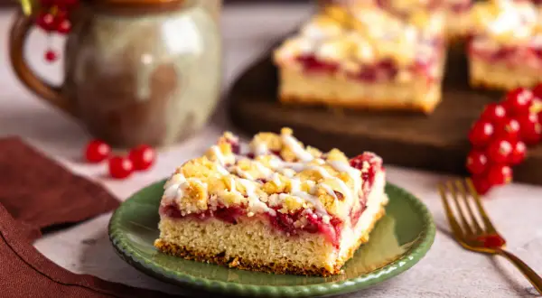 Saftiger Johannisbeerkuchen mit Streuseln, wie ihn Landfrauen backen. Ein Stück auf grünem Teller, daneben rote Johannisbeeren.